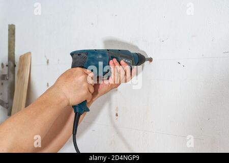 Un lavoratore sta perforando un buco nella parete con un trapano a percussione Foto Stock