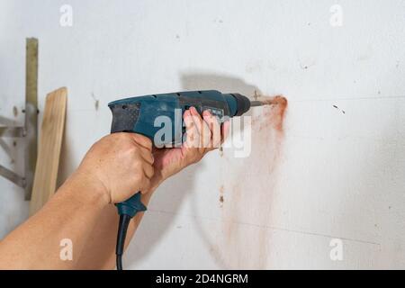 Un lavoratore sta perforando un buco nella parete con un trapano a percussione Foto Stock