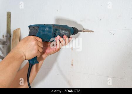 Un lavoratore sta perforando un buco nella parete con un trapano a percussione Foto Stock