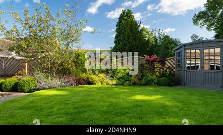 Giardino privato paesaggistico e soleggiato (design contemporaneo, piante di confine estive, capanna estiva, palle di topiario tagliate, prato) - Yorkshire, Inghilterra, Regno Unito. Foto Stock