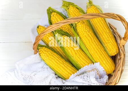 Mais fresco sulla pannocchia nel cesto di vimini. Pannocchie di mais non trattate. Verdure di mais fresche in cestino. Mais raccolto in paniere di vimini, spighe di mais appena raccolte ou Foto Stock