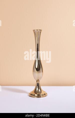 Vaso in ottone vintage con molta lucentezza e forma ricurva su un tavolo bianco e sfondo beige. Stile moderno di metà secolo, interni in oro Foto Stock