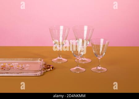 Set di eleganti bicchieri da cocktail martini in piedi accanto a un piatto da portata di vetro su una superficie marrone e uno sfondo rosa. Pulito minimalista ed elegante Foto Stock
