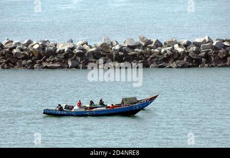 Vecchie barche da pesca in legno blu con gente del posto che si dirigono verso il terreno di pesca vicino al porto di Conakry in Guinea. Foto Stock