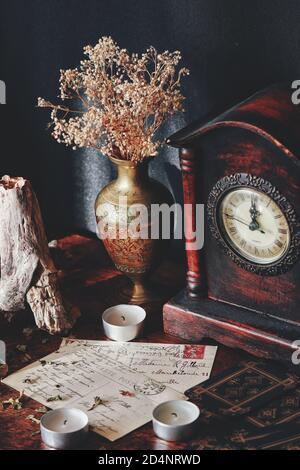 Cartoline d'epoca con corsivo corsivo scritto a mano su un tavolo di legno scuro. Atmosfera rustica con candele, vecchio orologio antico, vaso in ottone usurato Foto Stock