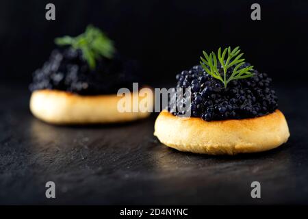 Cracker con caviale nero su ardesia scura Foto Stock