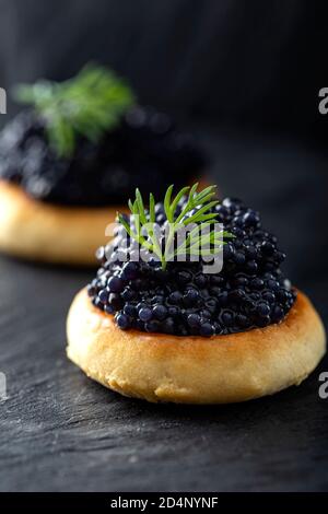 Cracker con caviale nero su ardesia scura Foto Stock