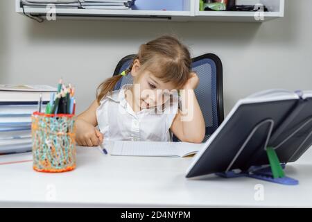 stanca bambina seduta su una scrivania e tenendo le mani a testa. bambino 4-5 anni. sulla scrivania un sacco di libri. Foto Stock