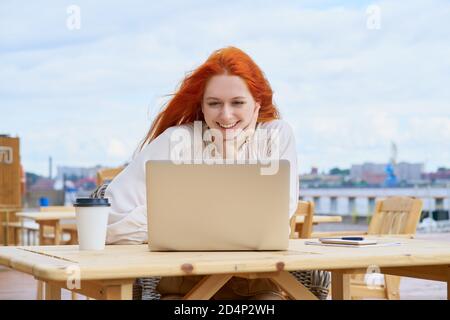Donna freelance che si trova in un bar sulla strada e lavora a distanza su un computer portatile. Corsi di ascolto studenteschi femminili Foto Stock