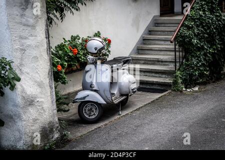 Lonely Vespa Scooter Iwrith un casco sul bar in un villaggio italiano di fronte a fiori rossi, scale e un muro Foto Stock