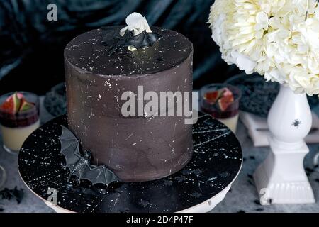 Torta di Halloween nera, decorata con pipistrelli e fiori. Un vaso con un bouquet di crisantemi bianchi e idrangee. In background sono cagliati Foto Stock