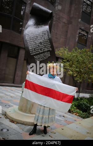 Una donna in piedi davanti al Suffragette Memorial a Victoria, Londra, che detiene una bandiera storica di uno stato bielorusso indipendente, dopo la rottura dell'impero russo, prima di marciare in solidarita con le donne della Bielorussia a Downing Street, Londra. Foto Stock