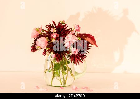 Un bouquet meraviglioso di fiori d'autunno come Dahlia Chat Noir E Rose Fairy in una caraffa di vetro verde con un sfondo bianco/rosa Foto Stock