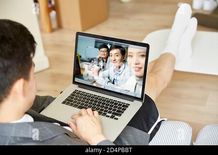 giovane uomo asiatico che lavora da casa incontro online con un team di persone aziendali tramite videoconferenza utilizzando un computer portatile Foto Stock