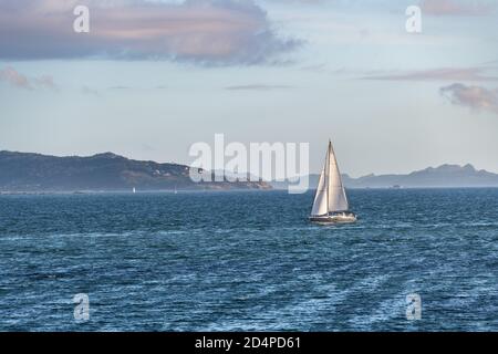 Una barca solitaria si allontana dalla Ria de Pontevedra in Galizia al tramonto, con le Isole Cies sullo sfondo. Foto Stock