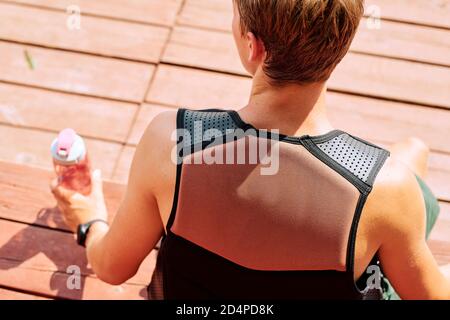 Vista posteriore del giovane sportivo con giacca di sicurezza che prende la bottiglia di acqua a rottura Foto Stock