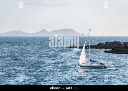 Una barca solitaria si allontana dalla Ria de Pontevedra in Galizia al tramonto, con le Isole Cies sullo sfondo. Foto Stock