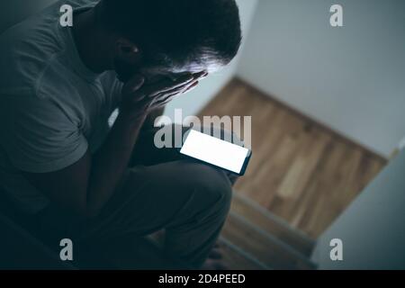 Uomo depresso seduto al buio con il suo smartphone Foto Stock