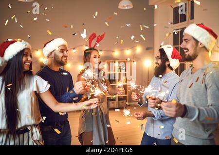 Amici con sparklers che si augurano buon Natale e felice Capodanno durante la festa a casa Foto Stock