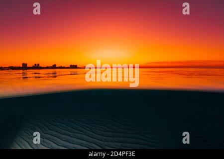 Vista divisa con tramonto luminoso e fondale marino sabbioso sottomarino. Foto Stock