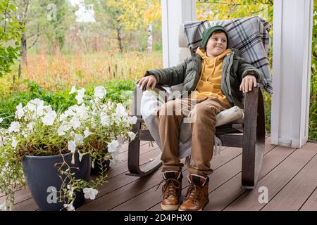 Felice rilassato scolaro in caldo casualwear seduto in sedia dondolo nel patio Foto Stock