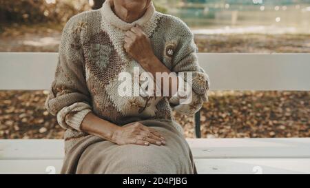 Donna anziana con pugno sopra il petto in dolore seduta sulla panchina nel parco in autunno. Foto di alta qualità Foto Stock