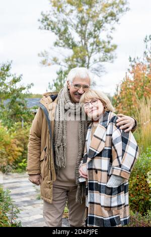 Felice affettuoso uomo anziano in caldo casualwear in piedi vicino al suo moglie bionda Foto Stock