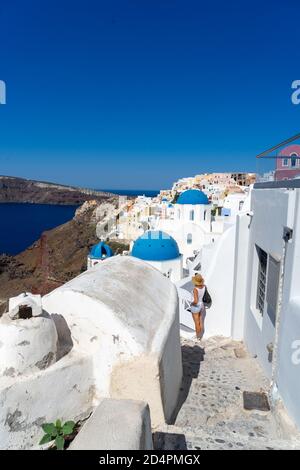 Donna che scatta a Santorini, con la tipica chiesa a cupola blu, vecchie case bianche e caldera. Paesaggio greco in una giornata di sole Foto Stock