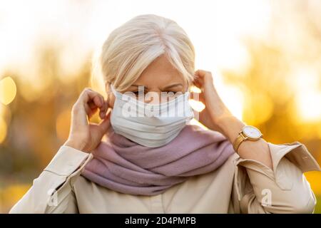 Donna anziana che indossava una maschera protettiva all'aperto Foto Stock