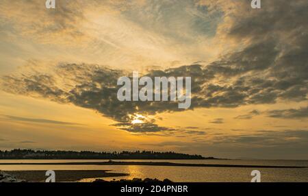 Guardando l'orizzonte verso Parksville Community Beach, il sole è nascosto dalle nuvole e si nutre di una tonalità giallo arancio sopra la città. Foto Stock