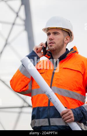 Un giovane ingegnere che parla con uno smartphone di fronte a un carro di perforazione o cantiere - mettere a fuoco sul viso Foto Stock