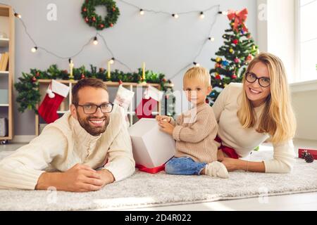 Ritratto di mamma felice, papà e figlio con regalo di Natale guardando la fotocamera durante la foto di famiglia Foto Stock