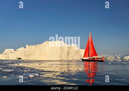 Barca a vela rossa di fronte a iceberg, Icefjord, patrimonio dell'umanità dell'UNESCO, Baia di Disko, Ilulissat, Groenlandia occidentale, Groenlandia, Nord America Foto Stock