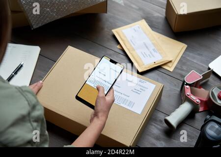 Lavoratore di magazzino femminile che esegue la scansione del codice a barre sulla scatola di spedizione sullo smartphone. Foto Stock