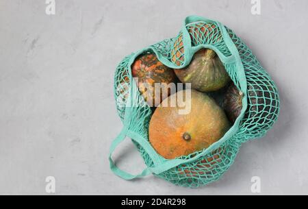 Varie zucche colorate in borsa a rete a filo turchese su sfondo chiaro, Zero Waste Concept, Copia spazio, Vista dall'alto. Foto Stock