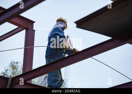 Operaio di costruzione in elmetto giallo con barra di acciaio di rinforzo. Il volto di nessun lavoratore. Foto Stock