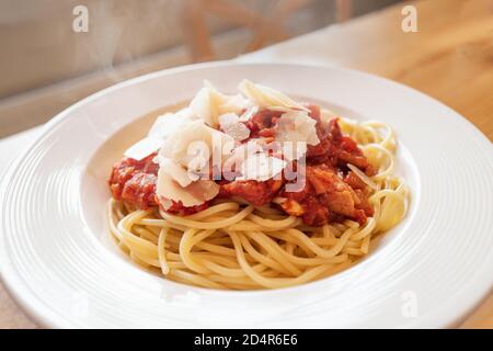 Spaghetti cotti in casa con salsa di pomodoro, pancetta e aglio, con aggiunta di scaglie di parmigiano. È possibile vedere il vapore proveniente dagli alimenti caldi. Foto Stock