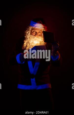 Attore maschile vestito come Babbo Natale che posa su uno sfondo rosso scuro. Foto Stock