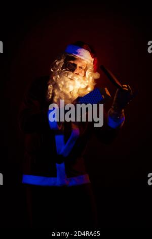 Attore maschile vestito come Babbo Natale che posa su uno sfondo rosso scuro. Foto Stock