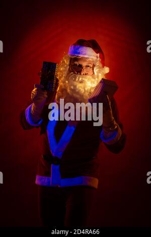 Attore maschile vestito come Babbo Natale che posa su uno sfondo rosso scuro. Foto Stock