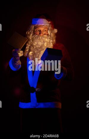 Attore maschile vestito come Babbo Natale che posa su uno sfondo rosso scuro. Foto Stock