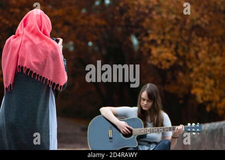 Ragazza musulmana che scatta foto di giovane ragazza mentre suona la chitarra Foto Stock