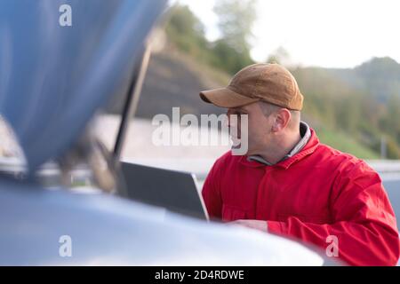 Bello auto meccanico o assistenza stradale lavoratore in uniforme di riparazione motore del Broken auto sulla strada Foto Stock