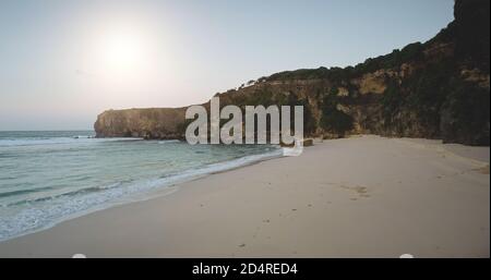 Luce del sole spiaggia di sabbia a Ocean Bay onde vista aerea. Incredibile mare con costa rocciosa e pietre. Isola di Sumba, paesaggio indonesiano durante il sole giorno d'estate. Luce solare soffusa sulle pareti rocciose Foto Stock