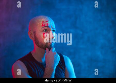 Ritratto di uomo pensivo con il trucco fluorescente incandescente sul viso in luce al neon. Concetto etnico, esoterico e artistico. Foto Stock