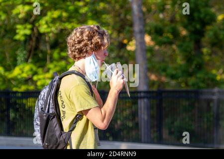 Ellicott City, MD, USA 10/07/2020: Un uomo caucasico biondo che indossa la maschera facciale a causa di COVID-19 sta rimuovendo temporaneamente parte della sua maschera per prendere un sorso Foto Stock