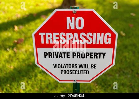Primo piano immagine isolata di un cartello ottagonale di metallo rosso e bianco che dice 'Proprietà privata, 'No Trespassing' 'i violatori saranno prosecutu Foto Stock