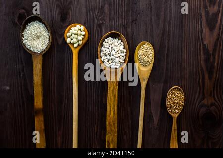 Vista dall'alto di cucchiai di legno su cui si trova un assortimento di cereali diversi su un tavolo di legno. Foto Stock