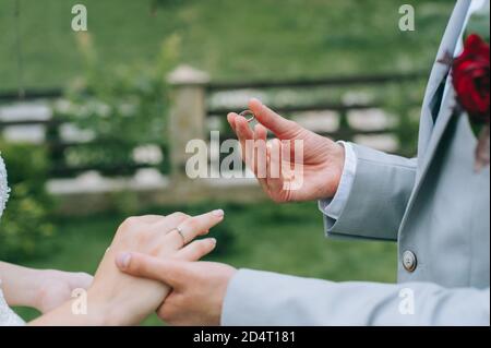 Mani di sposa e di sposo in solenne processo di scambio anelli che simboleggiano la creazione di una nuova famiglia Foto Stock