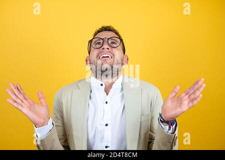 Giovane bel uomo d'affari che indossa vestito su isolato sfondo giallo senza clueless e l'espressione confusa con braccia e mani sollevate Foto Stock